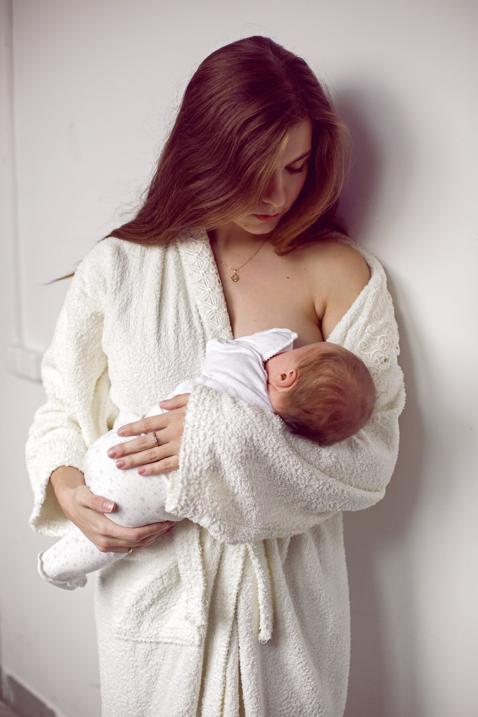 Mother in cozy white robe breastfeeding infant
