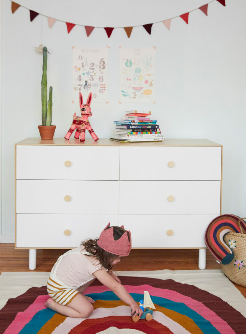 Child playing on Oeuf Rainbow Rug in front of Oeuf Fawn Dresser
