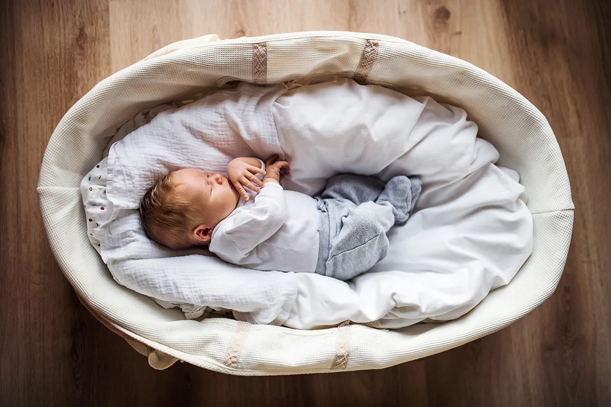 Baby sleeping in a Moses basket that would be classified as unsafe according to sleep guidelines from the American Academy of Pediatrics